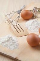 ägg, mjöl, kakform och visp på träplatta