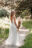glad brud flicka i en vit ljus klänning med en bukett torkade blommor foto