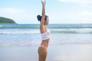 ung asiatisk kvinna i bikini gör yoga på stranden, hälsa och meditation koncept foto