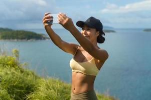 vacker asiatisk kvinna i sportkläder som tar foto på bergstoppen vid havet efter vandring, resor och ekoturismkoncept.