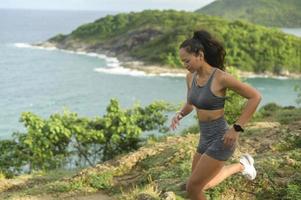 vacker vältränad kvinna i sportkläder som springer över stenstigen på bergstoppen vid havet, hälsa och resekoncept. foto