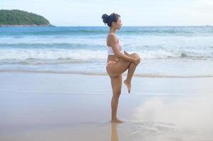 ung asiatisk kvinna i bikini gör yoga på stranden, hälsa och meditation koncept foto