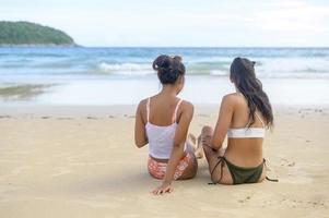 två attraktiva kvinnliga vänner i bikini njuter och kopplar av på stranden, sommar, semester, semester, livsstilskoncept. foto