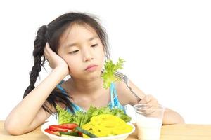 asiatisk härlig flicka visar tråkigt uttryck med färska färgglada grönsaker och ett glas mjölk isolerad över vit bakgrund foto
