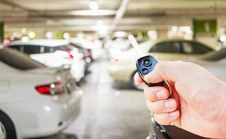en manhand trycker på bilfjärrnyckeln för att öppna - stäng sin bil på parkeringsplatsen foto