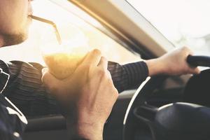 mannen dricker farligt en kopp kallt kaffe medan han kör bil foto
