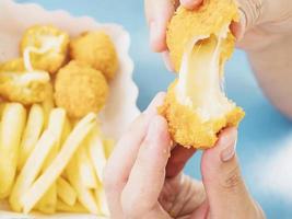 handen håller en stretch ostboll redo att ätas med mjuka fokuserade pommes frites på blå bordsbakgrund foto