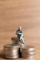 miniatyrmänniskor en affärsman sitter på toppen av en hög med pengar foto