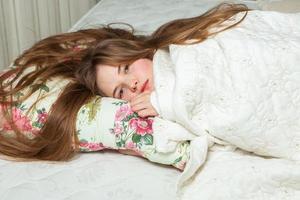 flicka sover i en vit säng hemma. ung kvinna sover i nattkläder på det vita linnet i sängen hemma, ovanifrån. foto