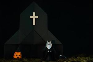 halloweenbakgrunden av origami eller pappersvikning som nunnan står framför svart kyrka med jack o lantern och spindel med stökig gräsmatta på svart bakgrund. foto