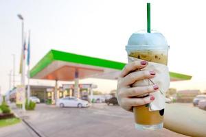 kvinnor hand som håller iskaffe med suddiga morgon tankstation bakgrund foto