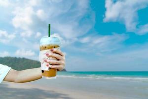 kvinnor hand som håller iskaffe med oskärpa havsutsikt och ön bakgrund foto