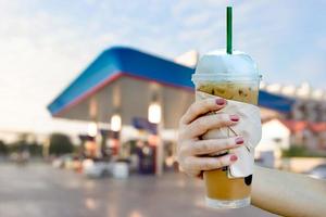 kvinnor hand som håller iskaffe med suddiga morgon tankstation bakgrund foto