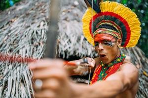 indian från pataxo-stammen med hjälp av pil och båge. brasiliansk indian med fjäderhuvudbonad och halsband foto
