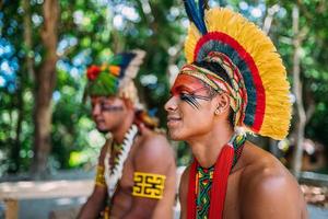 två indianer från pataxostammen. brasiliansk indian från södra Bahia med fjäderhuvudbonad, halsband och traditionella ansiktsmålningar som ser till vänster foto