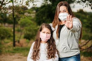 porträtt av ung mamma med ung dotter med mask. mor och dotter bär mask för att skydda covid-19, karantän. hand med stoppskylt. stanna hemma koncept. foto