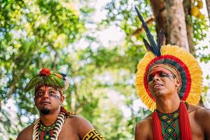 två indianer från pataxostammen. brasiliansk indian från södra Bahia med fjäderhuvudbonad, halsband och traditionella ansiktsmålningar som ser till vänster foto