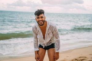 vänlig självsäker och leende ung latinamerikansk man tittar på kameran på stranden foto