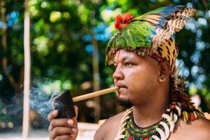 indianhövding från pataxostammen röker pipa. brasiliansk indian med fjäderhuvudbonad och halsband foto