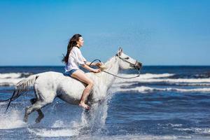 ung flicka rider på den vita hästen genom havet. foto