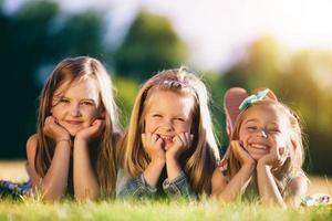 tre leende små flickor som ligger på gräset i parken. foto