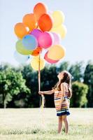 liten flicka som håller ett gäng färgglada ballonger i parken. foto