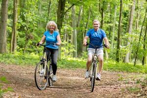 två äldre personer som cyklar i skogen. foto