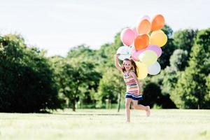 ung flicka kör på gräsfältet med ballonger. foto