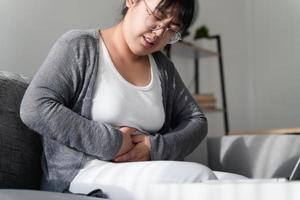 kvinna som lider av magvärk sitter i soffan hemma. buksmärtor, gastrit, mens, menstruation. foto