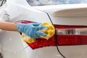kvinna hand bär blå handskar med gul svamp tvätt bakljus modern bil eller rengöring bil. biltvätt koncept foto