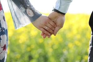 förälskade par håller händerna i grönt fält på sommaren. närbild foto