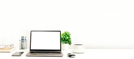 ett fungerande koncept med teknik, bärbar dator, smartphones, enheter. tom vit skärm laptop på ett vitt bord på kontoret. kopiera utrymme till höger för design eller text, närbild, grå och oskärpa bakgrund foto