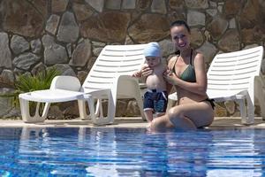 ung mamma, en vacker flicka och ett barn i en uppblåsbar cirkel för barn, i en blå pool på semester. foto