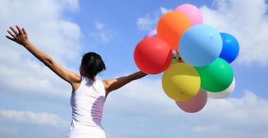 jublande kvinna med färgglada ballonger mot blå himmel foto