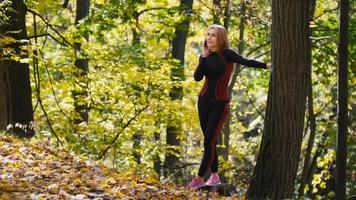 ung, sportig kvinna pratar i mobiltelefon på hösten park utomhus, ser till himlen foto