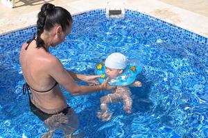 ung mamma, en vacker flicka och ett barn i en uppblåsbar cirkel för barn, i en blå pool på semester. foto