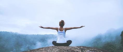 ung kvinna utövar yoga i bergen. asiatisk kvinna reser naturen. resa koppla av övningar yoga röra naturlig dimma på bergstoppen. foto