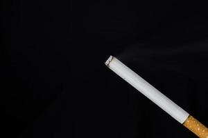 brinnande cigarett med rök på svart bakgrund foto