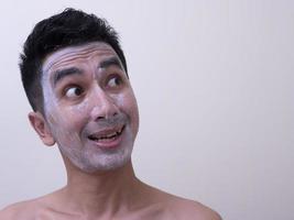 asiatisk stilig ung man applicerar grädde i ansiktet med smiley, hudvårdskoncept foto