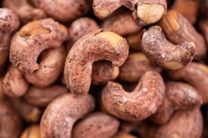 cashewnötter med skal i en tallrik på träbricka och bordsbakgrund, hälsosam raw food tallrik. foto