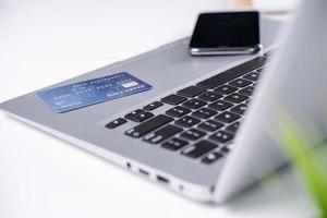 kontor online betalar, stanna hemma och handla, elektronisk betalning med kreditkortskoncept, bärbar dator på vit bordsbakgrund med butiksvagn, närbild. foto