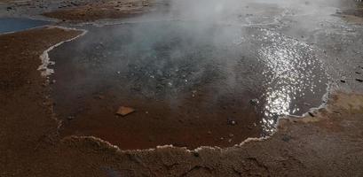 cool ångande geysir på Island omgiven av mineraler foto