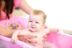 mamma tvättar en baby i rosa badkar foto
