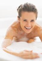 leende ung kvinna som leker med skum i badkaret