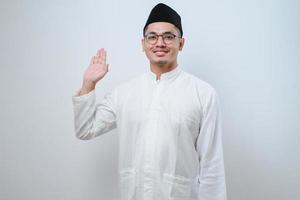 asiatisk muslimsk man som ler mot kameran medan viftar med handen säger hej foto