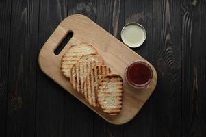 rostat bröd med hemgjord jordgubbssylt och på rustikt bord med smör till frukost eller brunch. foto