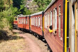 leksakståg rör sig på bergssluttningar, vacker utsikt, ena sidan berg, ena sidan dalen rör sig på järnväg till kullen, bland grön naturskog. leksakståg från kalka till shimla i indien, indiskt tåg foto