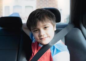 porträtt glad ung pojke som sitter i bilbarnstol och tittar på kameran med ett leende ansikte, barn som sitter i passagerarsätet bak med ett säkerhetsbälte, skolbarn som reser till skolan med bil. tillbaka till skolan foto