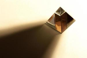 minimalistisk stillebenbild av en glänsande pyramid i varm färgton. pyramid kastar hård skugga. foto