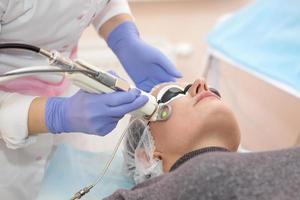terapeut kosmetolog gör en laserföryngring för kvinnan med apparater i en skönhetssalong. foto